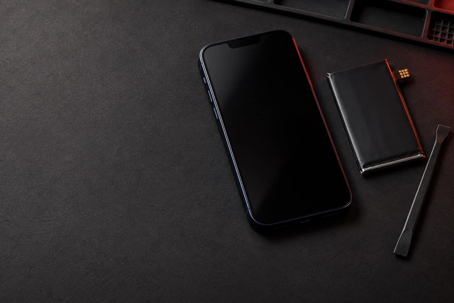 iPhone 13 color medianoche sobre un tapete de reparación, junto a una batería de repuesto y una espátula