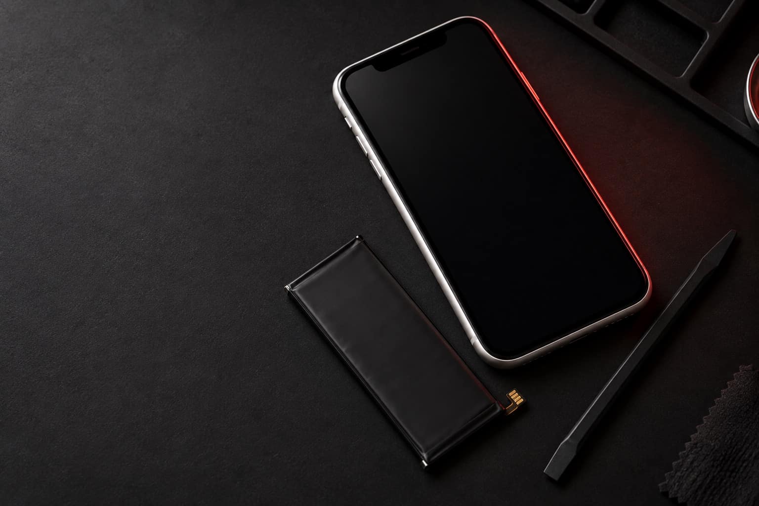 White iPhone XR on a repair mat with a replacement battery and a spudger