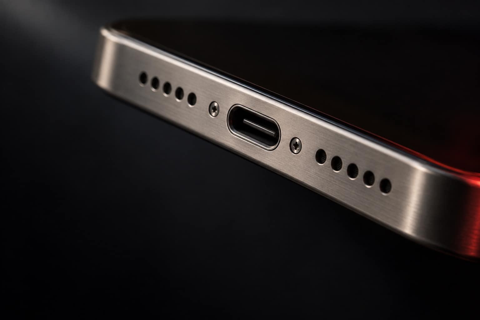 Bottom edge of a natural titanium iPhone 15 Pro Max showing the USB-C port and speaker grilles